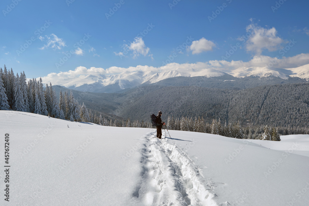 Man backpacker hiking snowy mountain hillside on cold winter day.