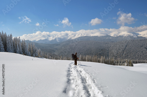 Man backpacker hiking snowy mountain hillside on cold winter day.