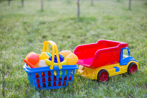 Car truckand a basket with toy fruit and vegetables. Bright plastic colorful toys for children outdoors on sunny summer day. photo