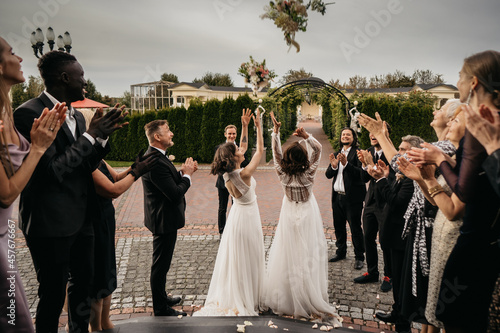 Candid shot of two female lesbian LGBT brides toss their bouquets over their shoulders to their guests photo