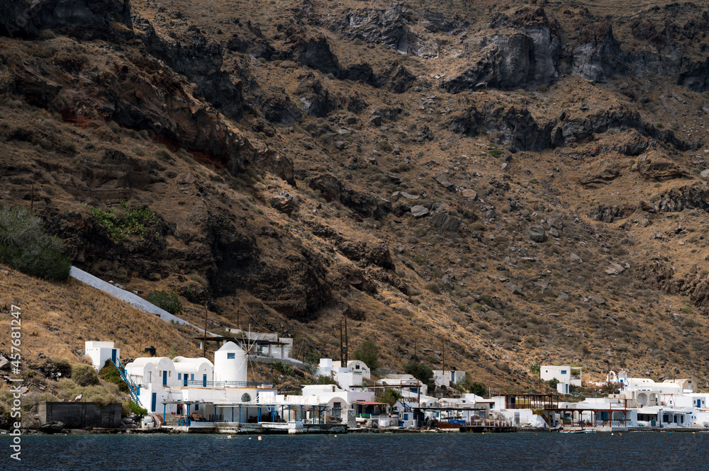 The white architecture of the island of Santorini on the seashore at the foot of the cliff.