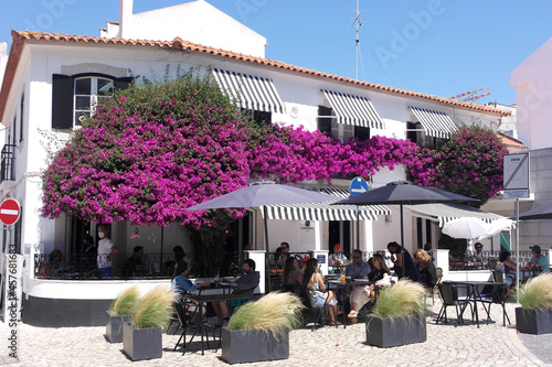 Portuguese lovely cafe terrace , white facade wall patio decorated with pink lush blooming flowers.