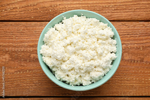 Delicious fresh cottage cheese in bowl on wooden table, top view