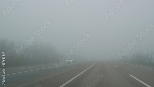 Cars move on foggy road, view through windshield in daytime. Cars pass through fog on road. Poor visibility in mist highway. Dangerous weather for driving. Cars keep distance at haze