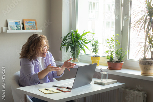 woman working at home with laptop and white table notebook pen and phone talking