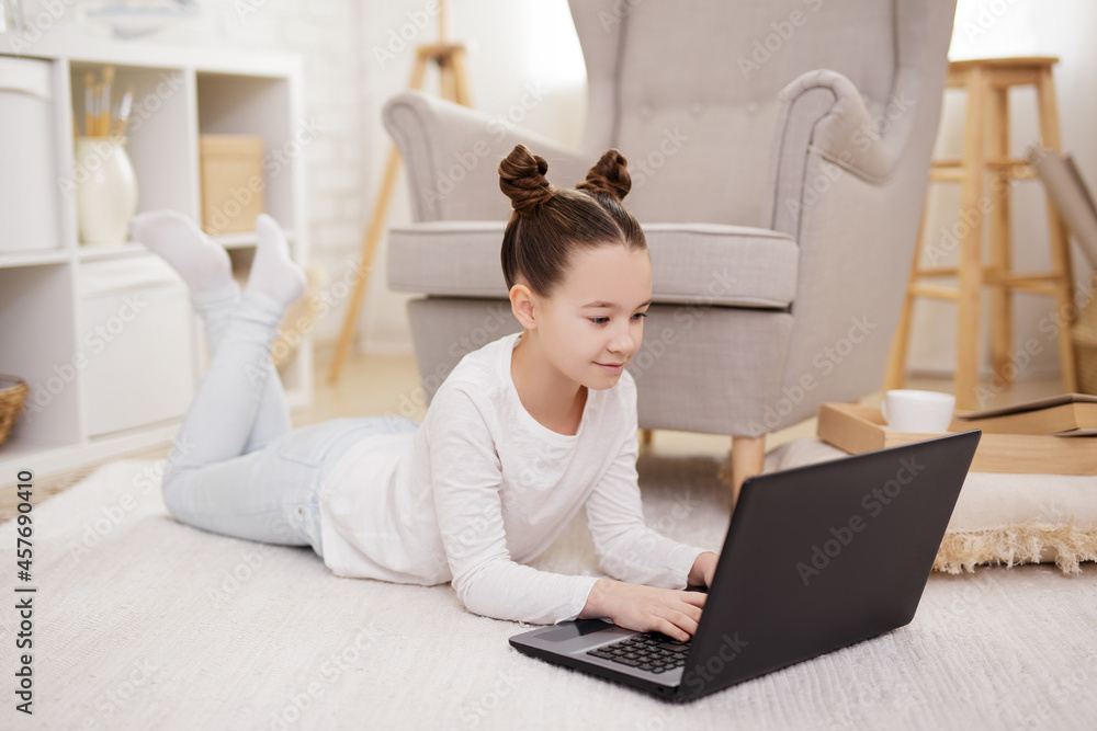 lifestyle, technology and online education concept - cute preteen girl using laptop in bright living room lifestyle, technology and online education concept - cute preteen girl using laptop in bright living room
