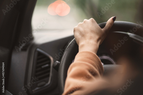 The woman's hands on the steering wheel of the car close-up. The girl is driving her car. Waiting for the driver in a traffic jam in the metropolis. A hand in a beige jacket holds the steering wheel