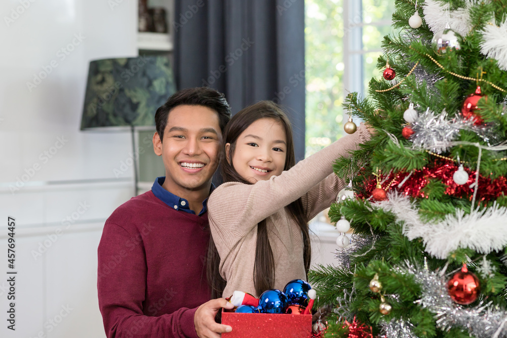Merry Christmas and holidays. Happy Asian young father and daughter decorating Christmas tree at home. Christmas celebration concept Merry Christmas and holidays. Happy Asian young father and daughter decorating Christmas tree at home. Christmas celebration concept