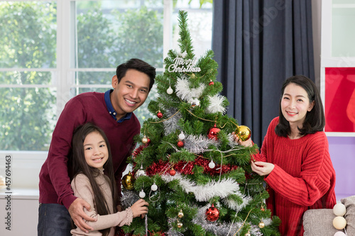 Merry Christmas, Happy young family and cute daughter little girl decorating Christmas tree at home, Christmas celebration concept © amorn