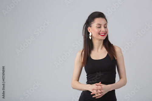 Beautiful young woman in little black dress looking away with happy smile. Pretty female model in 30s wearing classic evening dress and professional makeup with red lipstick