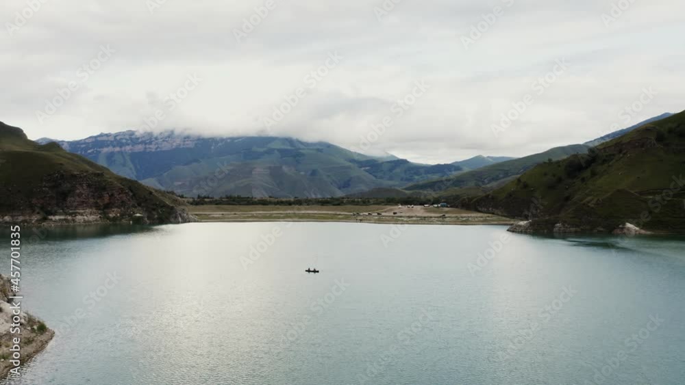 A man and a woman are sailing on a rowboat on a lake among rocky mountains A man and a woman are sailing on a rowboat on a lake among rocky mountains
