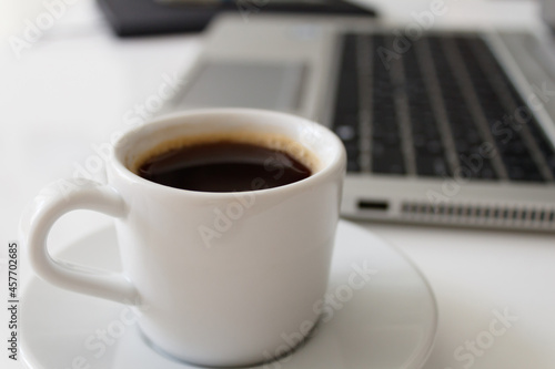 The concept of a workplace with coffee, a laptop and a notebook with a pen on a modern white office desk. Easy to use. Minimalism. Side view.