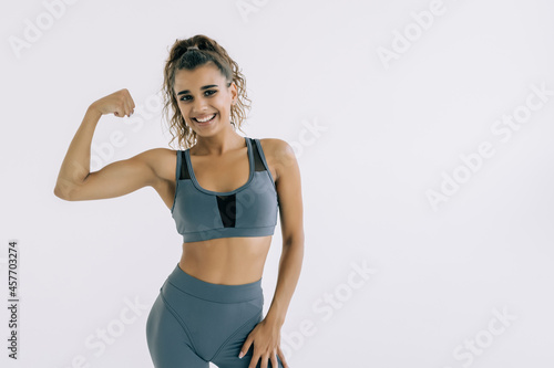 Cheerfully smiling sporty woman demonstrating biceps on white background © F8  \ Suport Ukraine