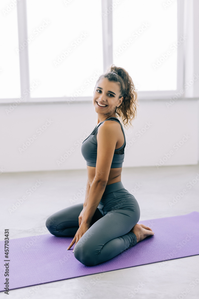 Fototapeta premium Fit woman resting in gym after a hard workout. Long haired caucasian coach sitting on yoga mat. Fitness concept.