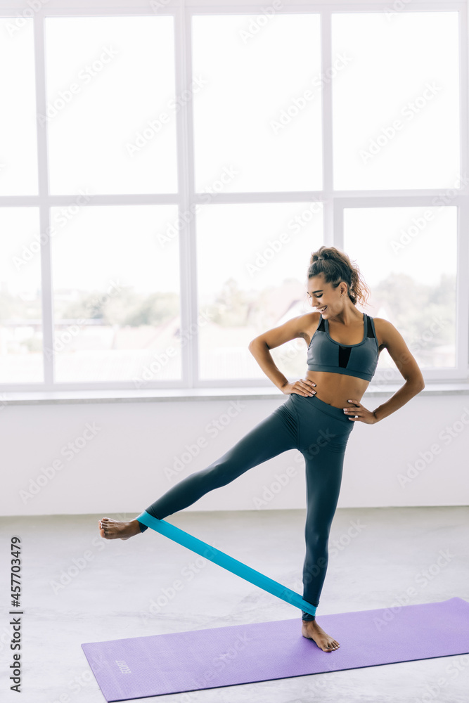 Resistance band fitness girl doing leg workout donkey kick floor exercises with rubber strap elastic.