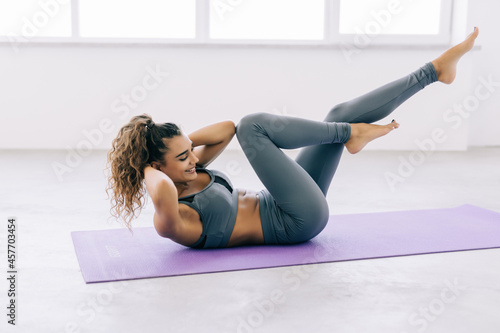 Young fit woman exercising in a gym lying on mat doing leg raising and twisting exercises. Young attractive woman doing abs workout. Fitness woman doing a sit up.