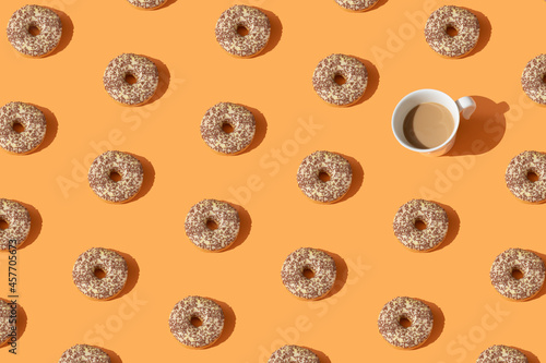 Donuts and a white cup of coffee on orange color background. Creative pattern sweet food concept. Dessert. Sweet dish. Layout. Top view. Flat lay.