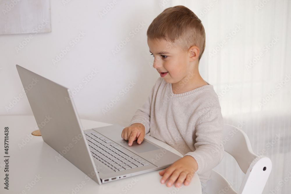 Happy little boy playing game on laptop at home. Portrait of a child at home watching cartoon on the computer. Modern kid and education technology. Happy little boy playing game on laptop at home. Portrait of a child at home watching cartoon on the computer. Modern kid and education technology.