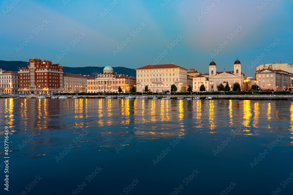 sea coast in Trieste Italy with beautiful illuminated buildings Saint Nicholas church and reflection on the water