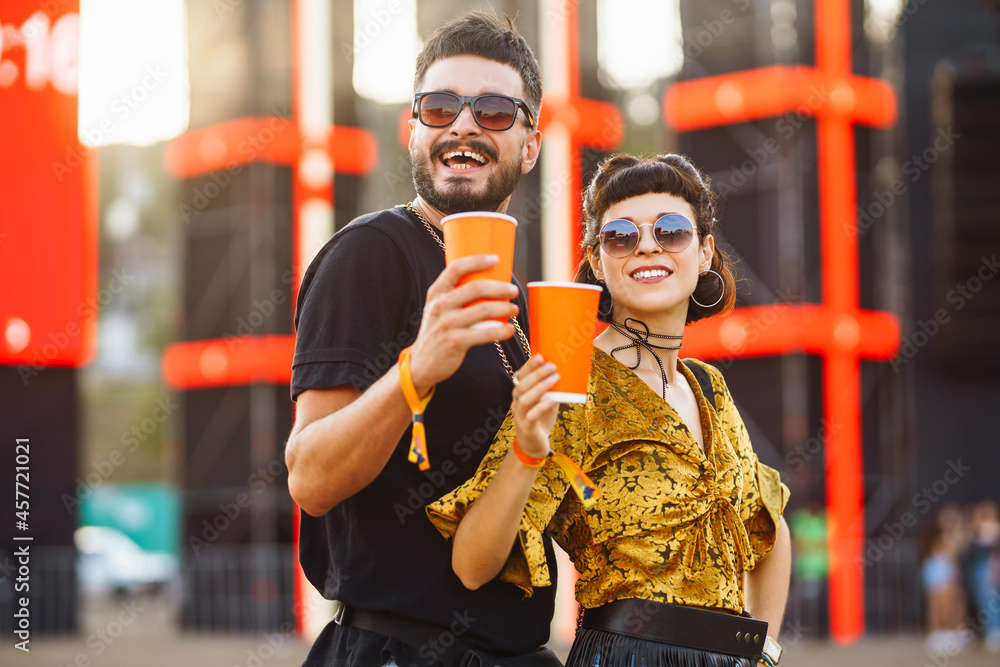 Stylish couple enjoying a performance at a festival together. Young people drinking beer and having fun at music festival at the beach. Youth, party, vacation concept.