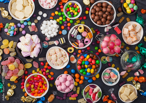 Quadro su tela Pink lollipop candies in jar with various milk chocolate and jelly gums candies on black background with liquorice allsorts and strawberry bonbons and large variety of sweets and candies