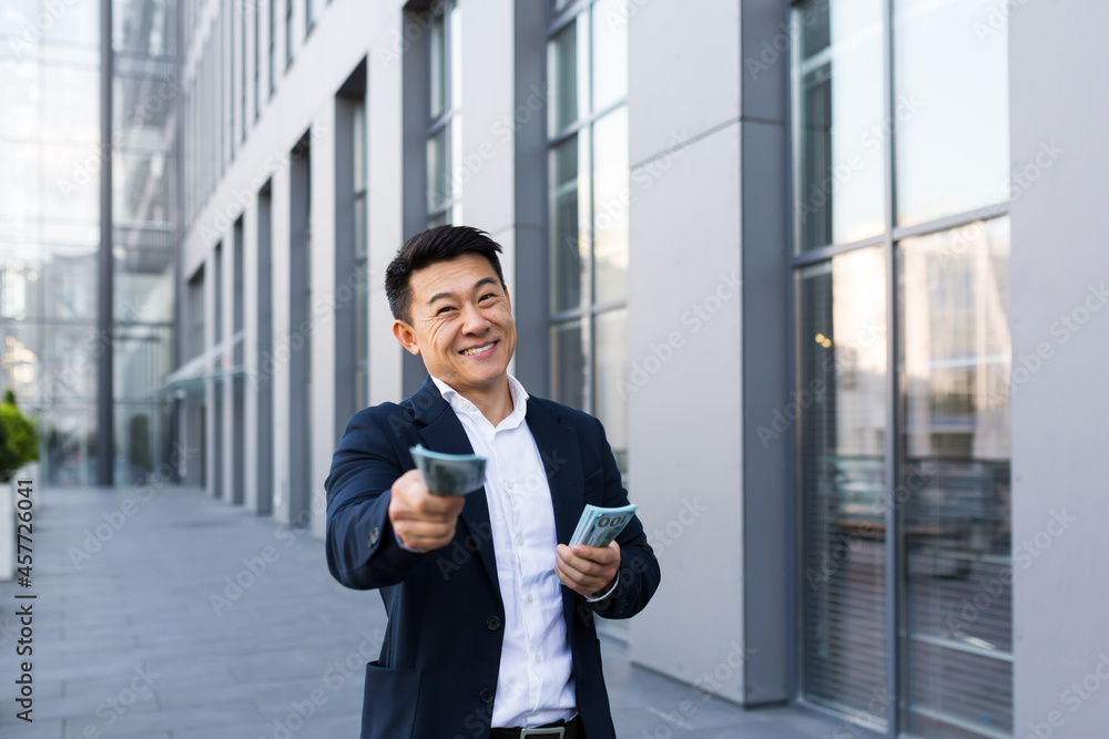 Male asian businessman rejoices holding a lot of cash looking at the camera giving money Male asian businessman rejoices holding a lot of cash looking at the camera giving money