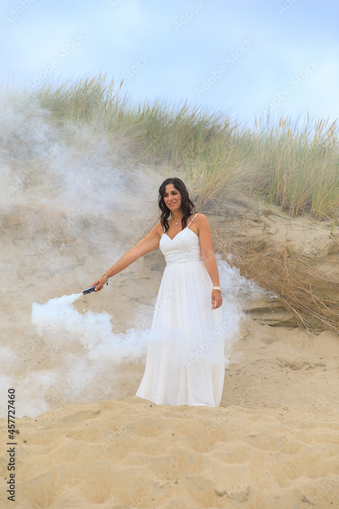 Junge schöne Frau im Hochzeitskleid am Strand mit einer Rauchfackel und weißen Rauch Junge schöne Frau im Hochzeitskleid am Strand mit einer Rauchfackel und weißen Rauch