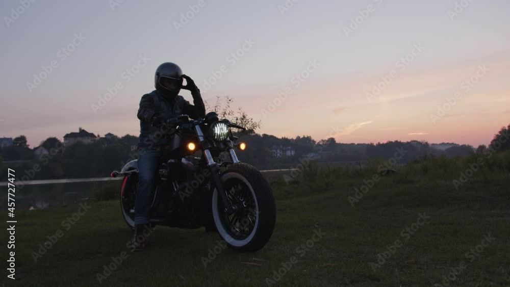 A stylish motorcyclist riding his custom motorcycle along the field road with the sunset sky in the background. A stylish motorcyclist riding his custom motorcycle along the field road with the sunset sky in the background.