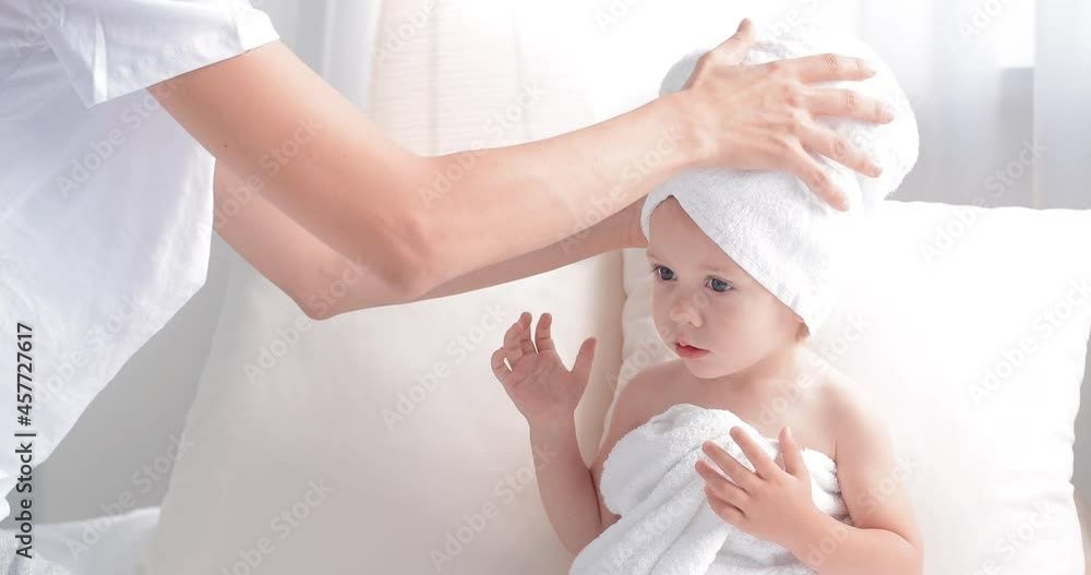 A little girl of two years old is resting after swimming. Mom wraps the baby in a towel after taking a bath A little girl of two years old is resting after swimming. Mom wraps the baby in a towel after taking a bath