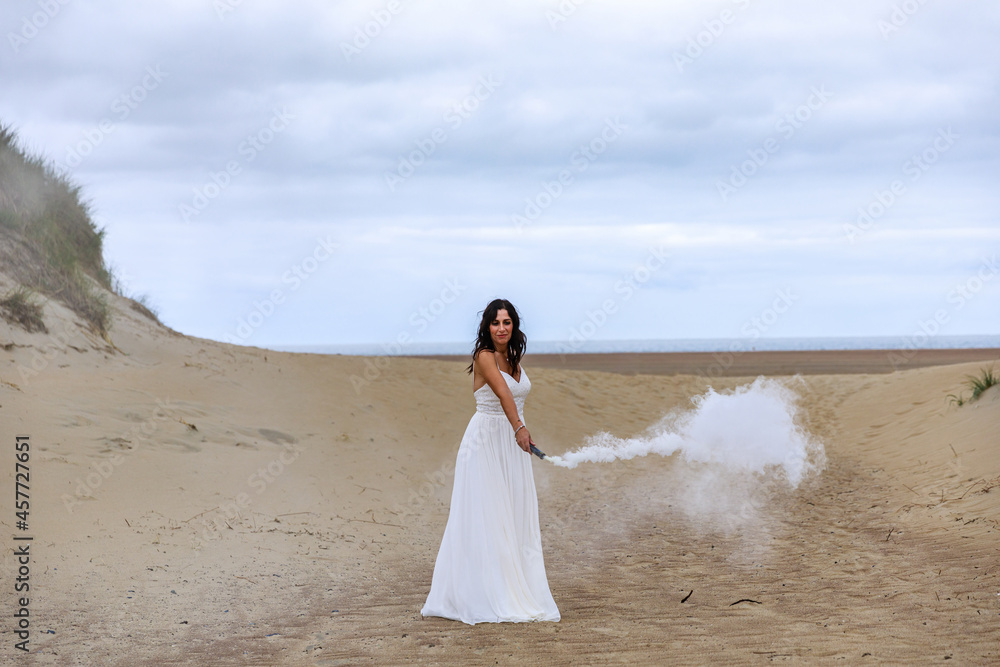 Junge schöne Frau im Hochzeitskleid am Strand mit einer Rauchfackel und weißen Rauch Junge schöne Frau im Hochzeitskleid am Strand mit einer Rauchfackel und weißen Rauch
