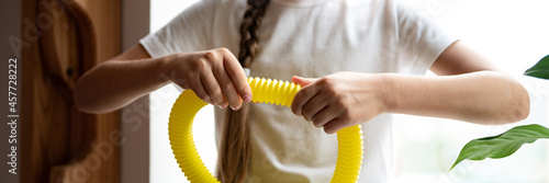 anti stress sensory pop tube plastic toy in a kid's hands. a little happy child girl plays with a poptube fidget toy at home. children holding and playing pop tube yellow color. banner photo