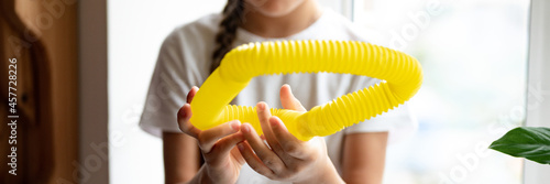 anti stress sensory pop tube plastic toy in a kid's hands. a little happy child girl plays with a poptube fidget toy at home. children holding and playing pop tube yellow color. banner photo