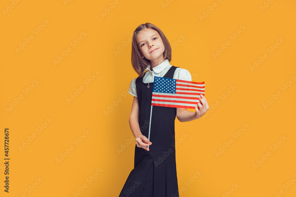 Beautiful smiling caucasian schoolgirl holds american flag in hands on yellow background. USA flag Beautiful smiling caucasian schoolgirl holds american flag in hands on yellow background. USA flag