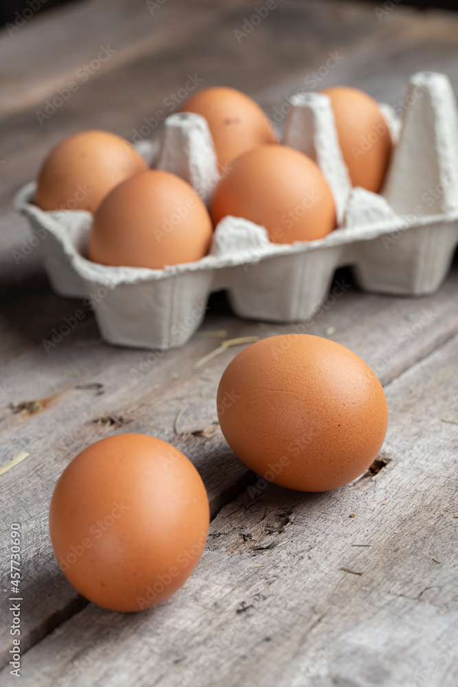 Brown eggs in a cardboard box. Eggs are scattered over a wooden background. Healthy food concept. Brown eggs in a cardboard box. Eggs are scattered over a wooden background. Healthy food concept.