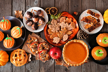 Autumn desserts table scene with a variety of sweet fall treats. Above view over a dark wood background.