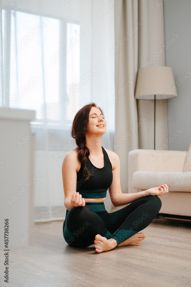 Young happy athlete in the lotus position is sitting on the floor of the house doing yoga. Young happy athlete in the lotus position is sitting on the floor of the house doing yoga.