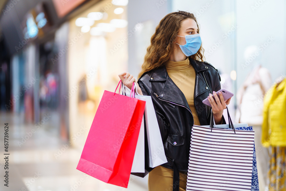 Stylish woman in protective medical mask with shopping bags using her phone. Autumn shopping. Fashion, style, Black friday, sale, consumerism concept.