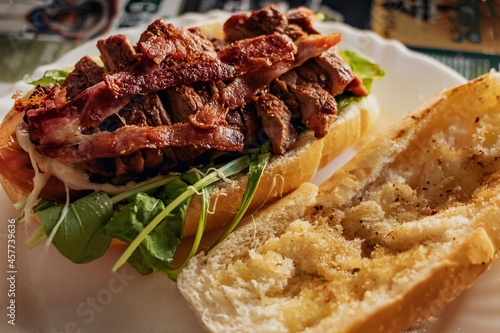 Sanduíche de carne e bacon com salada de rúcula exibindo o receio num prato em uma mesa de bar