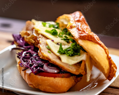 Sanduíche de panceta com queijo, salada de repolho roxo e fatias de tomate com recheio a vista sobre um prato em uma mesa