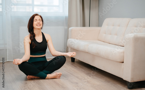 Young woman does yoga exercises indoors at home, meditating on a light background.Concept healthy lifestyle. Free Download Young woman does yoga exercises indoors at home, meditating on a light background.Concept healthy lifestyle. - GFXLoad