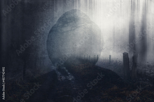 A double exposure of a scary hooded figure with no face. Over layered with a misty path on a winters day. With a blurred, grunge, vintage, abstract edit