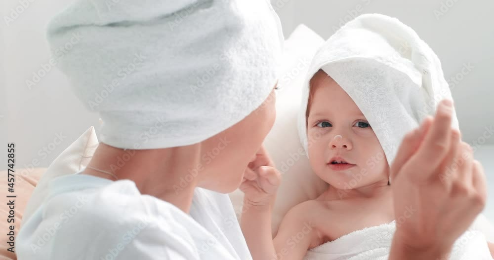 in slow motion. Mom and her little daughter are resting after a bath. Girls smear each other's noses with cream in slow motion. Mom and her little daughter are resting after a bath. Girls smear each other's noses with cream
