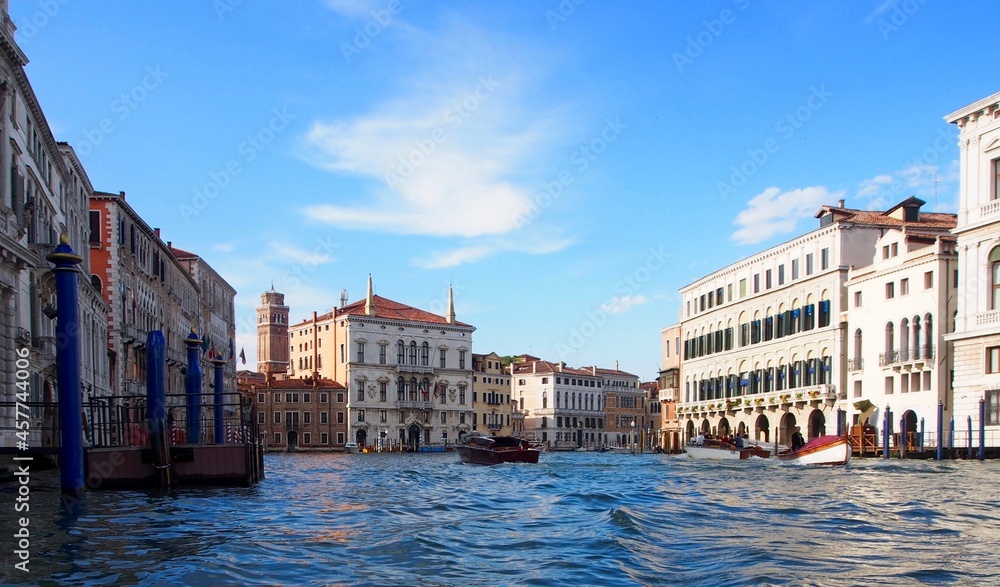 Venice, Italy - Grand Canal with blue sky and wispy clouds.  Palaces line the banks of the canal, and a speedboat navigates the center of the waterway. Horizontal with modern colors.