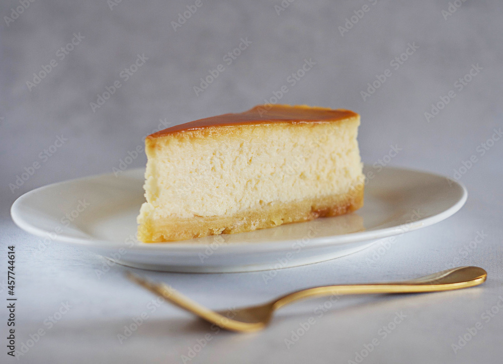 A piece of caramel cheesecake on a saucer on the table with a gold fork next to it.. A piece of caramel cheesecake on a saucer on the table with a gold fork next to it..