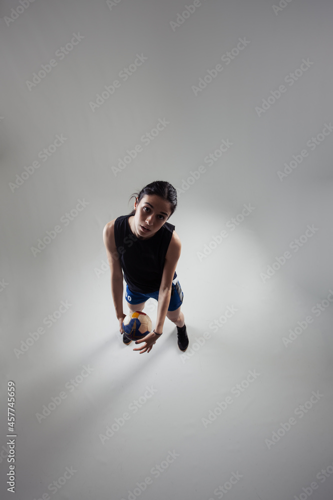 Handball player posing on light gray background. Girl posing with ball.