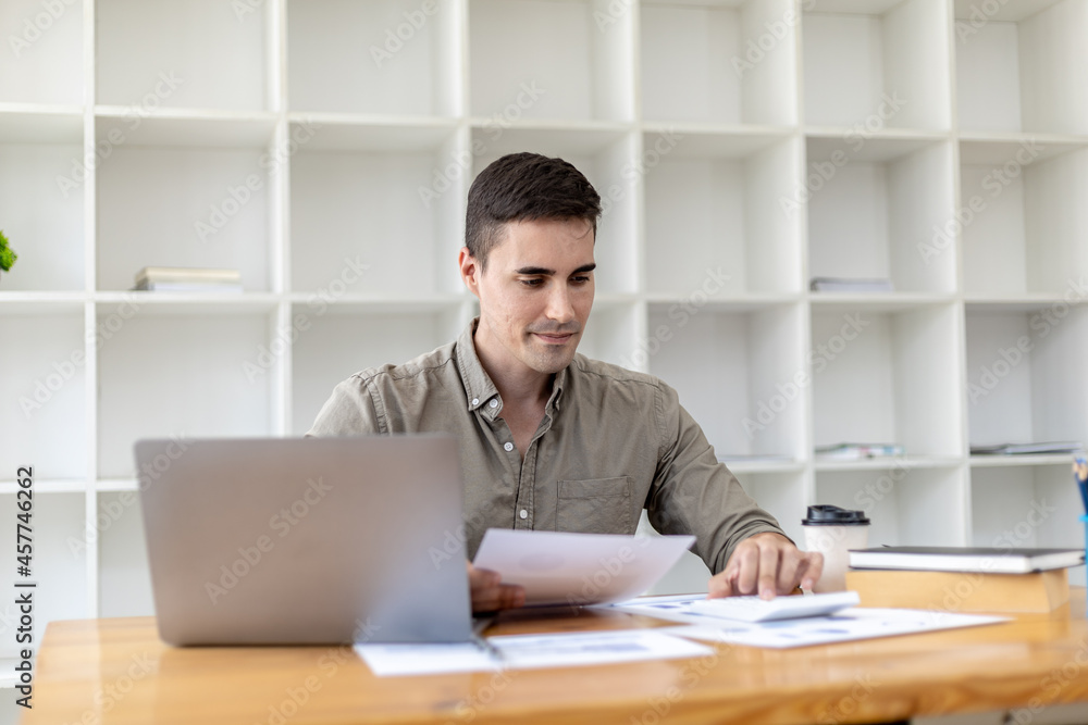 Young businessman sitting and checking financial documents displayed in chart format, young businessman who founded a startup company, managing a new business to grow by leaps and bounds.