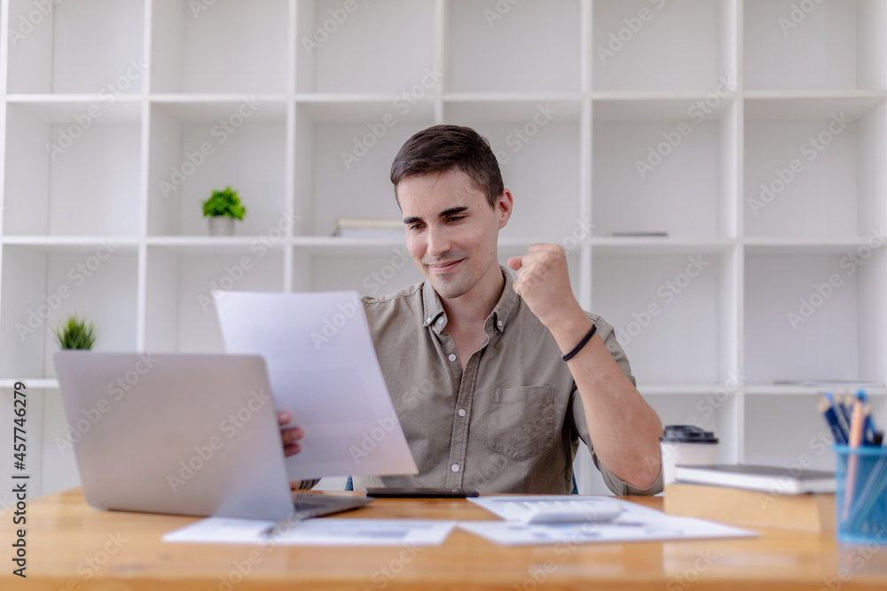 Fototapeta premium Young businessman sits in his office with a laptop, he looks delighted as he reads the documents that the company is profitable, he is a young businessman who is skilled in running the company to grow