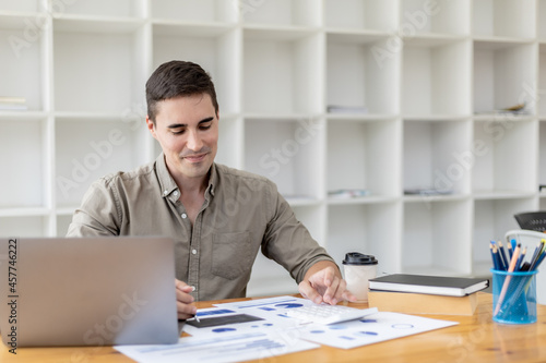 Young businessman sitting and checking financial documents displayed in chart format, young businessman who founded a startup company, managing a new business to grow by leaps and bounds.
