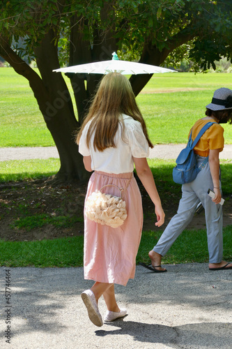 woman with white parasol walking in the park on a sunny day © Heidi Patricola