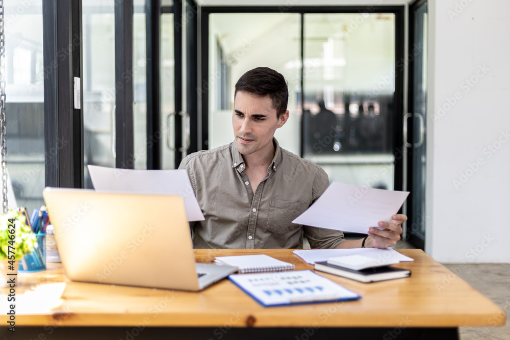 A businessman holding a sales document that the sales department summarizes, he looks displeased when he sees reports of falling sales, he shows signs of stress. Failed sales management concept. A businessman holding a sales document that the sales department summarizes, he looks displeased when he sees reports of falling sales, he shows signs of stress. Failed sales management concept.